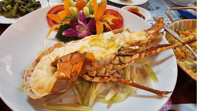 A beautifully presented plate of steamed seafood with vibrant red meat, served with a rich dipping sauce.